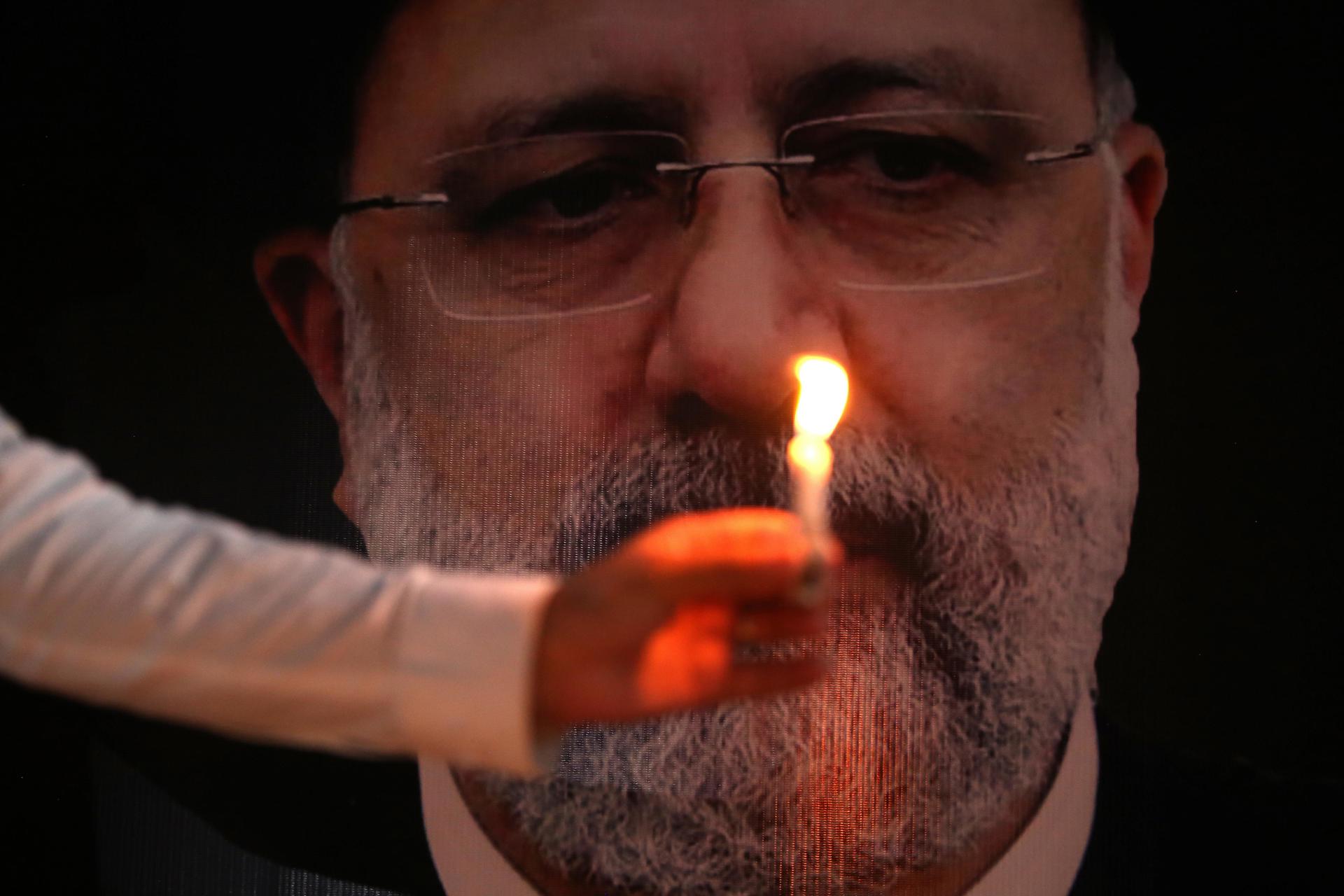 Un hombre sostiene una vela frente a una fotografía del fallecido presidente de Irán Ebrahim Raisi.